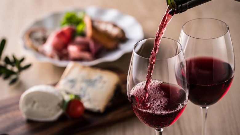 Two glasses of red wine with food in background