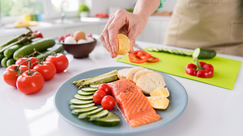 Woman's hand squeezes lemon onto a plate of salmon.