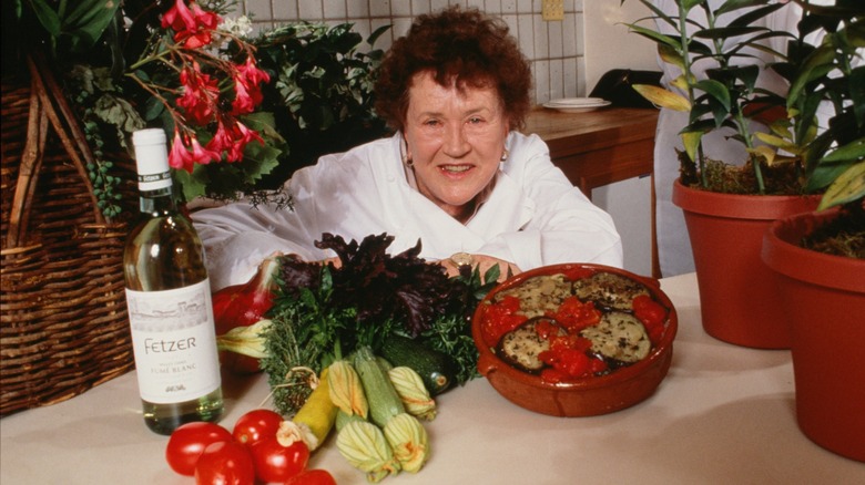 Julia Child posing behind a spread of food.