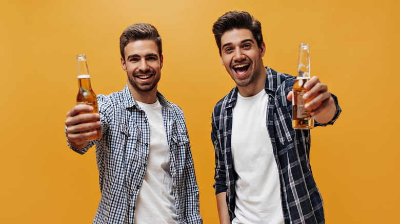 two men smiling holding bottled beer