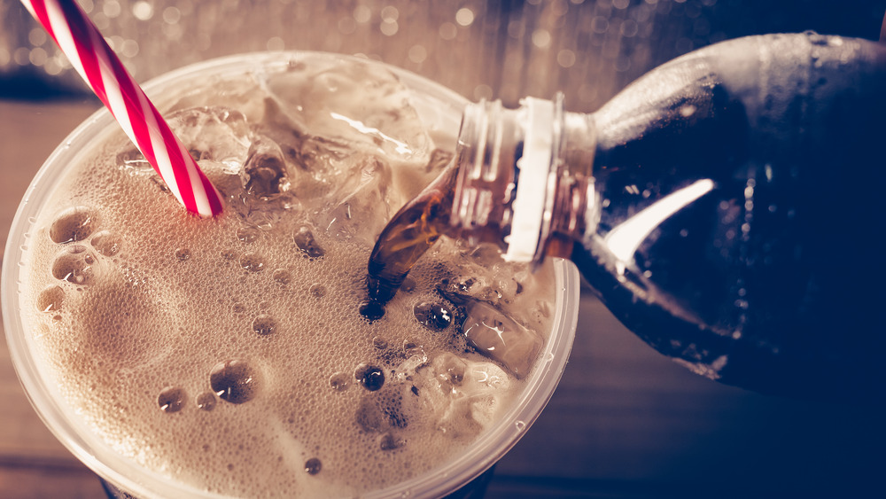 A dark soda being poured into a glass of ice