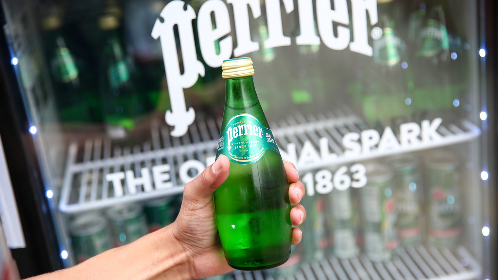 A hand holding a bottle of Perrier