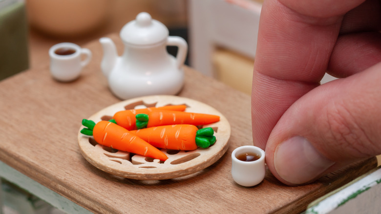 hand holding tiny coffee cup next to tiny carrots