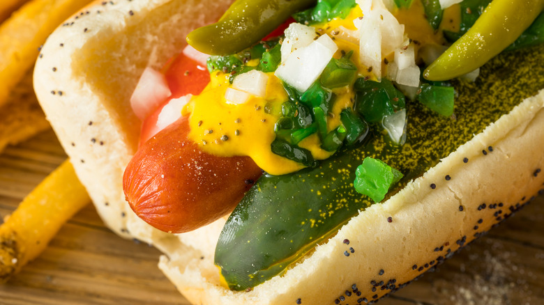 close of up Chicago style hot dog on poppy seed bun with yellow mustard, raw white onion, neon green relish, pickle, and celery salt