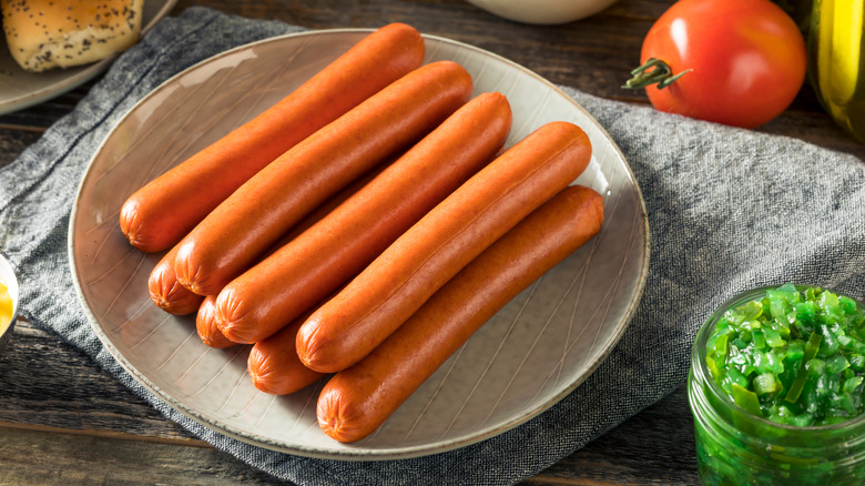 plate of uncooked beef hot dogs surrounded by other ingredients for Chicago style hot dogs including raw tomato and neon green relish