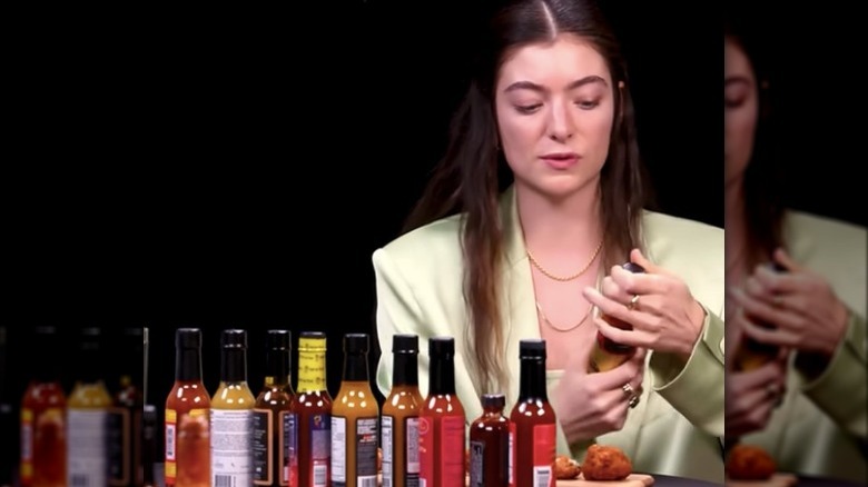 Lorde adding hot sauce to a wing