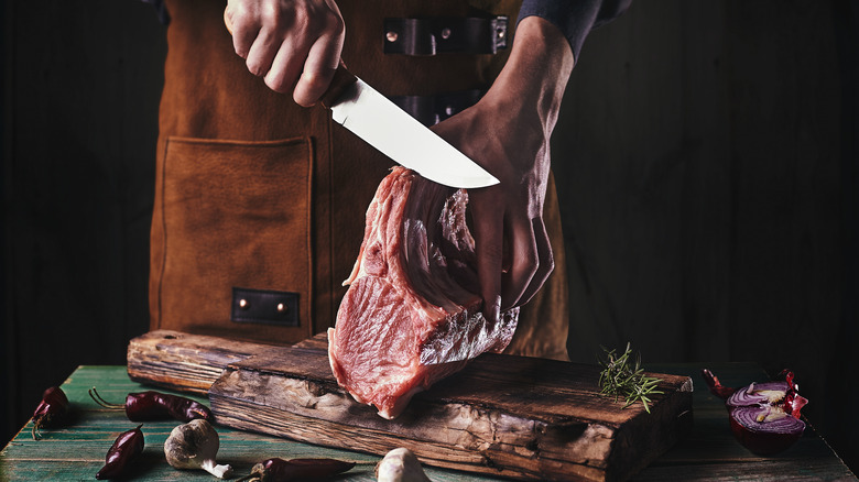 A person cutting into a slab of raw beef with a knife. 