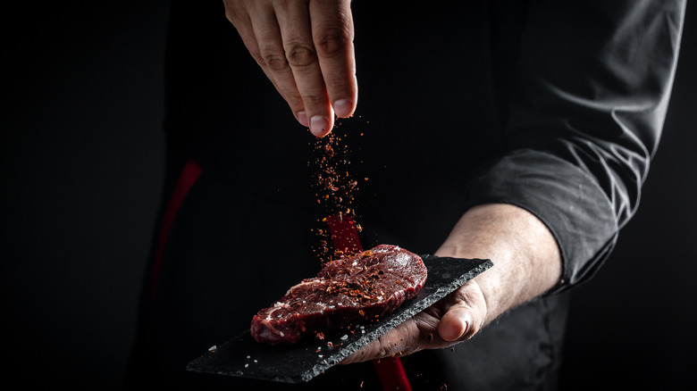 Chef hands seasoning beef steak. 