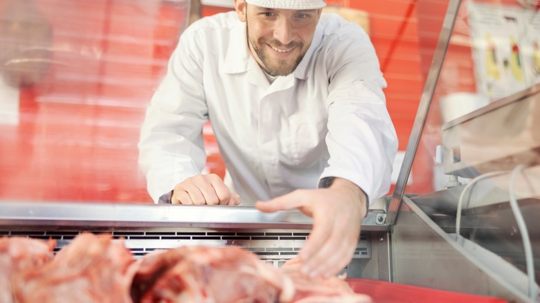 Smiling butcher reaches for meat