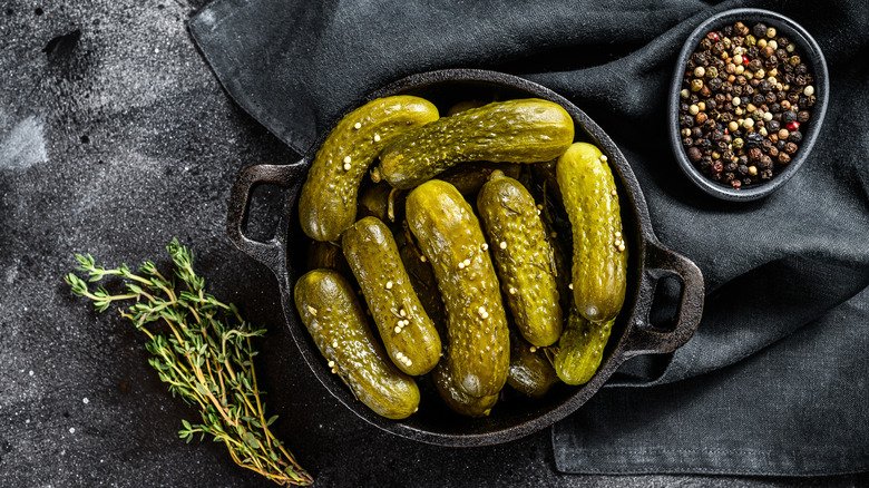 Dill pickles on a skillet next to herbs and black pepper