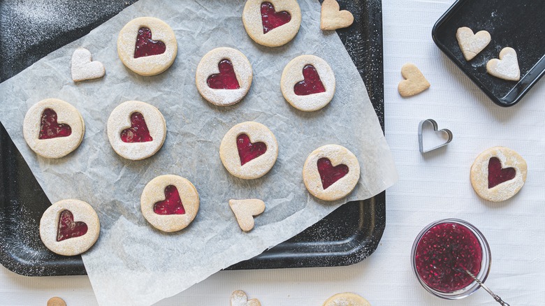 Linzer cookies on baking sheet with jam and cookie cutters