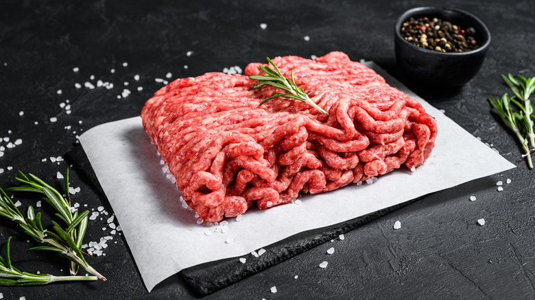 Ground beef on parchment with salt, rosemary, and peppercorns