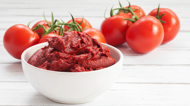 Tomato paste in white bowl with tomatoes in background