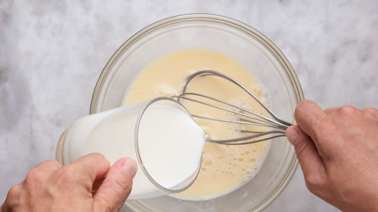 milk poured into bowl of whisked eggs