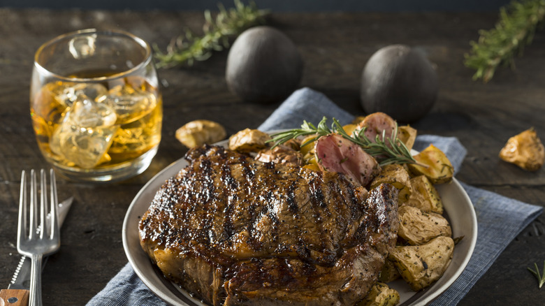 Glass of whiskey with steak and potatoes