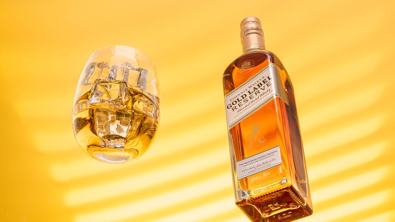 Bottle of Johnny Walker and a glass of alcohol with ice on a yellow background