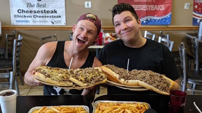 Two guys posing with cheesesteaks
