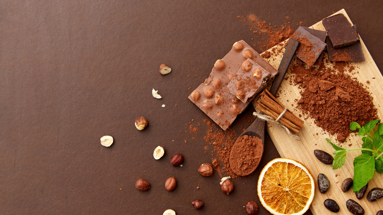 Cutting board with chocolate, spices, mint leaves, and orange slices on brown background