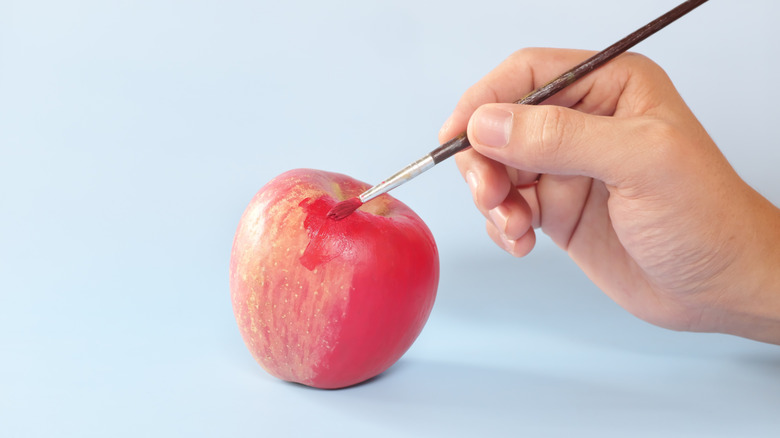 Hand with paintbrush painting apple