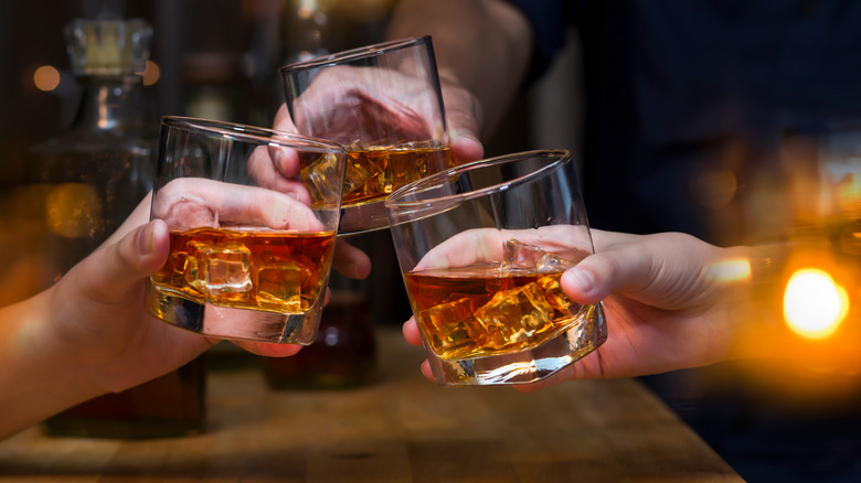 Three hands making a toast with bourbon on ice