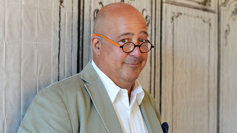 Andrew Zimmern smiling wearing glasses