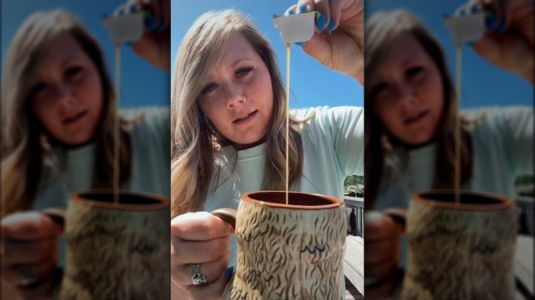 Person pouring sauce from fast food dip cup into mug