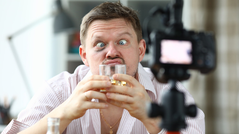 man smells a glass of whiskey improperly