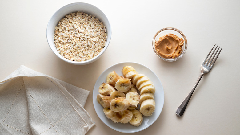 Bowl of oats, cup of peanut butter, and bowl of sliced bananas