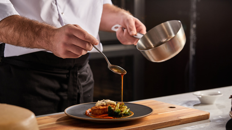 Chef pouring sauce from pan onto plate
