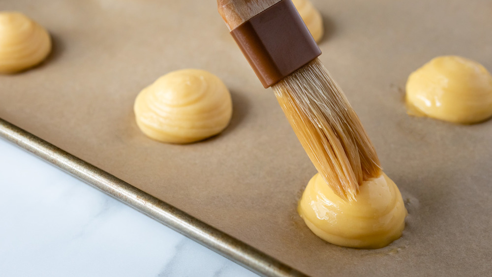 egg wash being brushed onto cream puffs