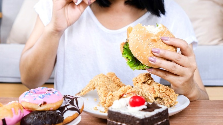 Woman eating burger, fried chicken, and donuts