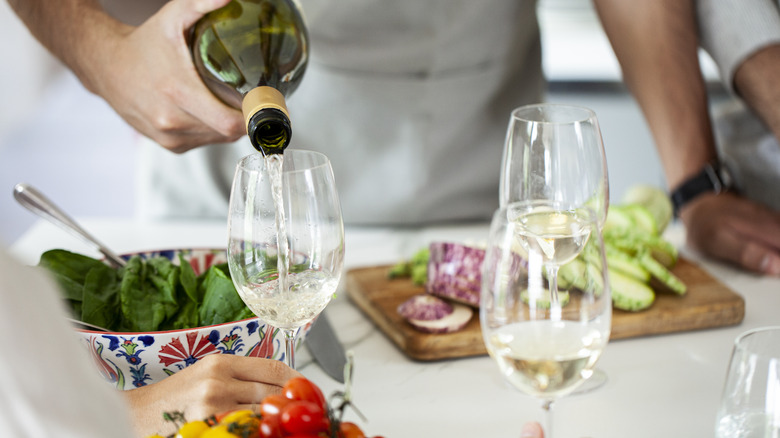 hand pouring wine with salad ingredients surrounding