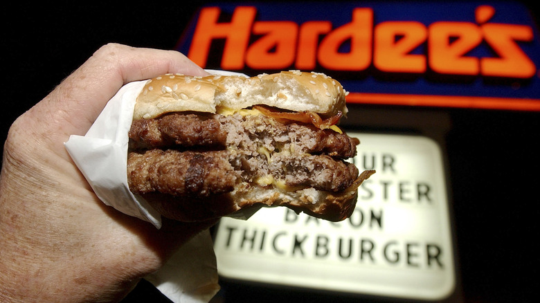 Hand holds a burger in front of Hardee's sign