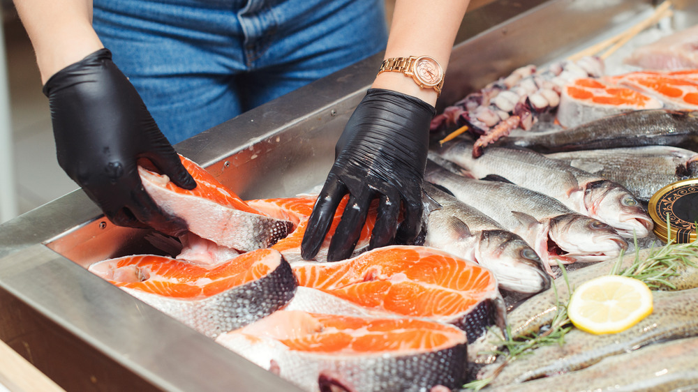 Person with black gloves handling cuts of seafood