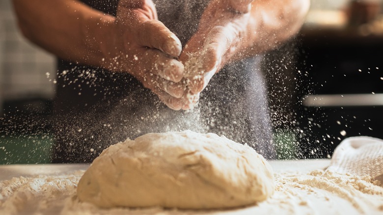 hands dusting flour on pizza dough