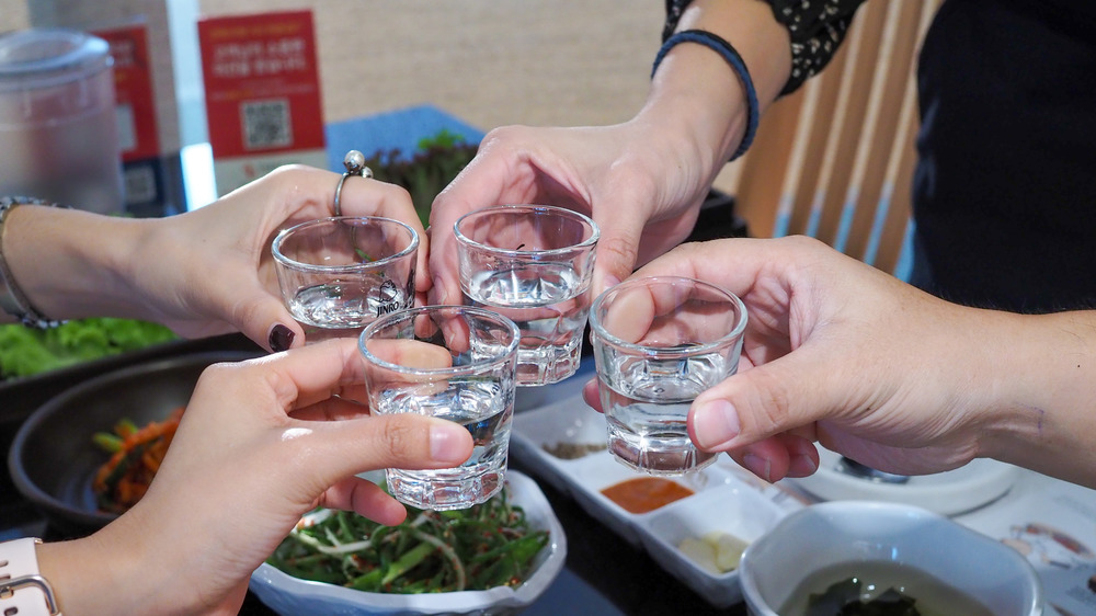 Four people toasting with soju in clear glasses