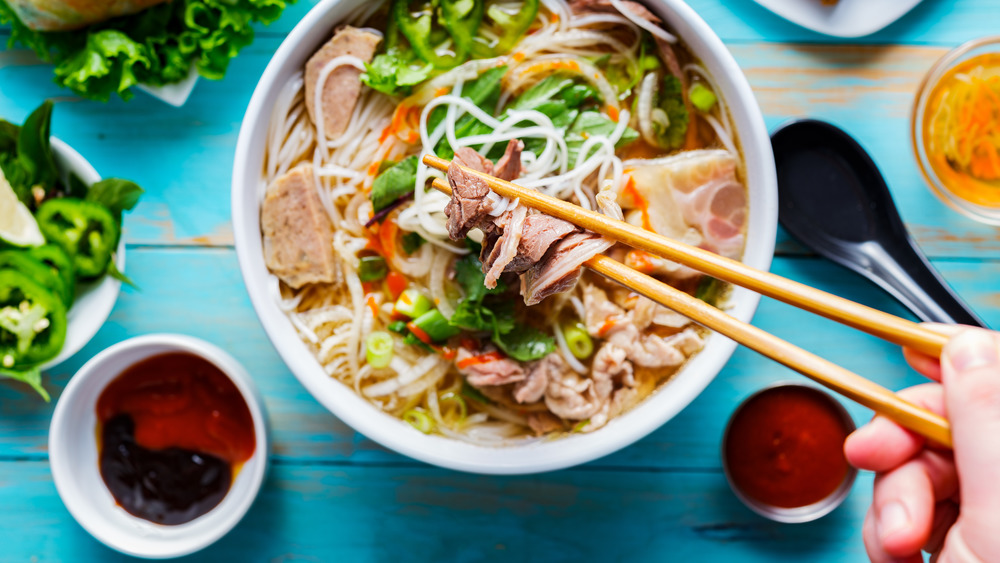 Small dishes of sauce next to bowl of pho