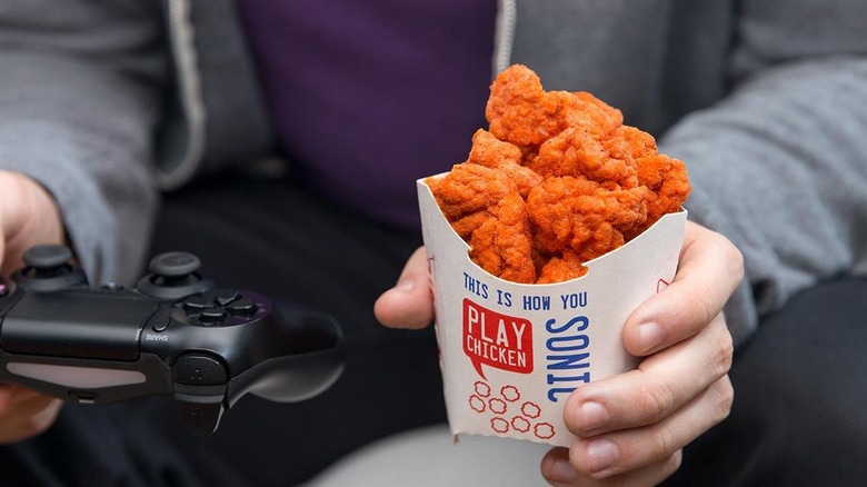 Man holding popcorn chicken and video game controller 