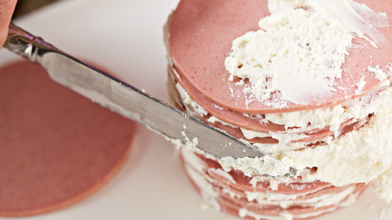 person frosting bologna cake with cream cheese