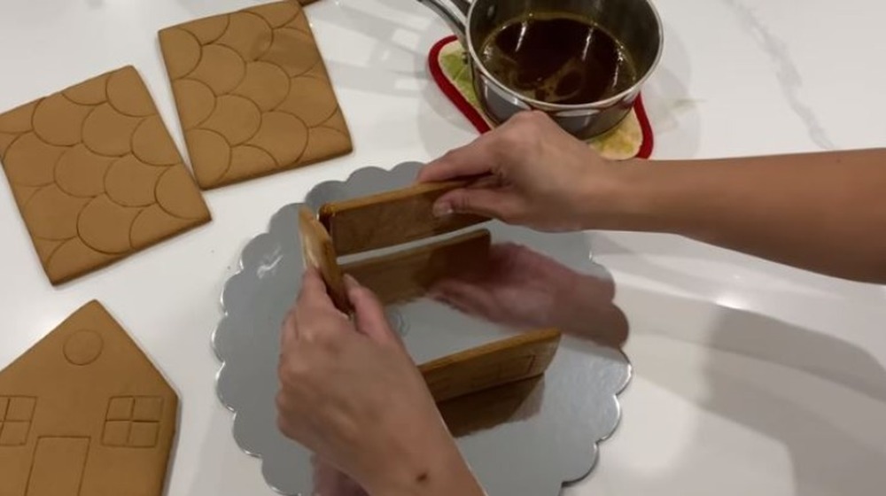 Person assembling gingerbread house using caramel