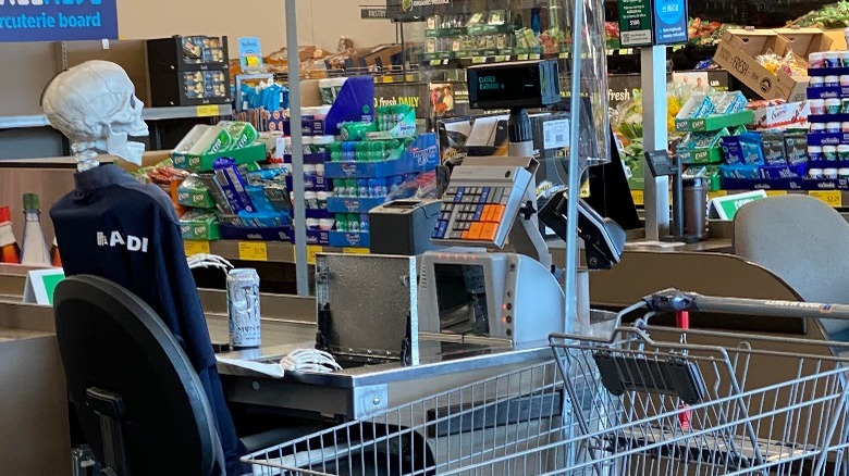 Kkeleton sitting in chair behind cash register at Aldi