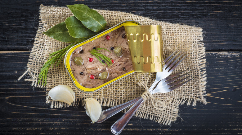 canned tuna dressed with various herbs and spices on a burlap and wooden surface