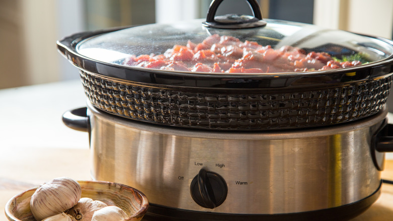 Slow cooker next to bowl of garlic