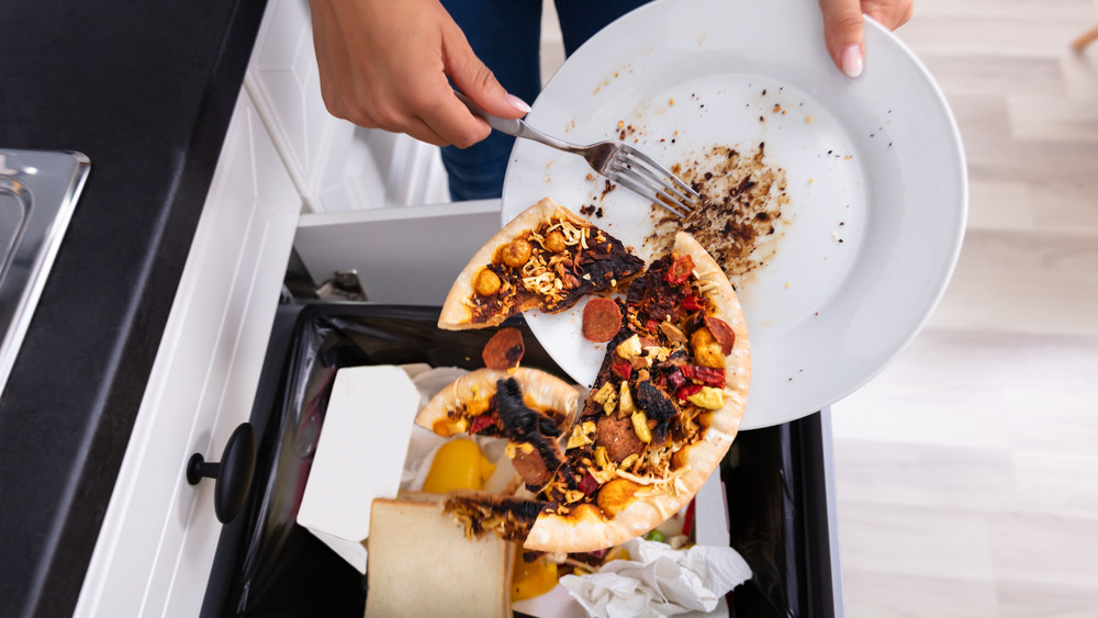 A person throwing away most of a pizza