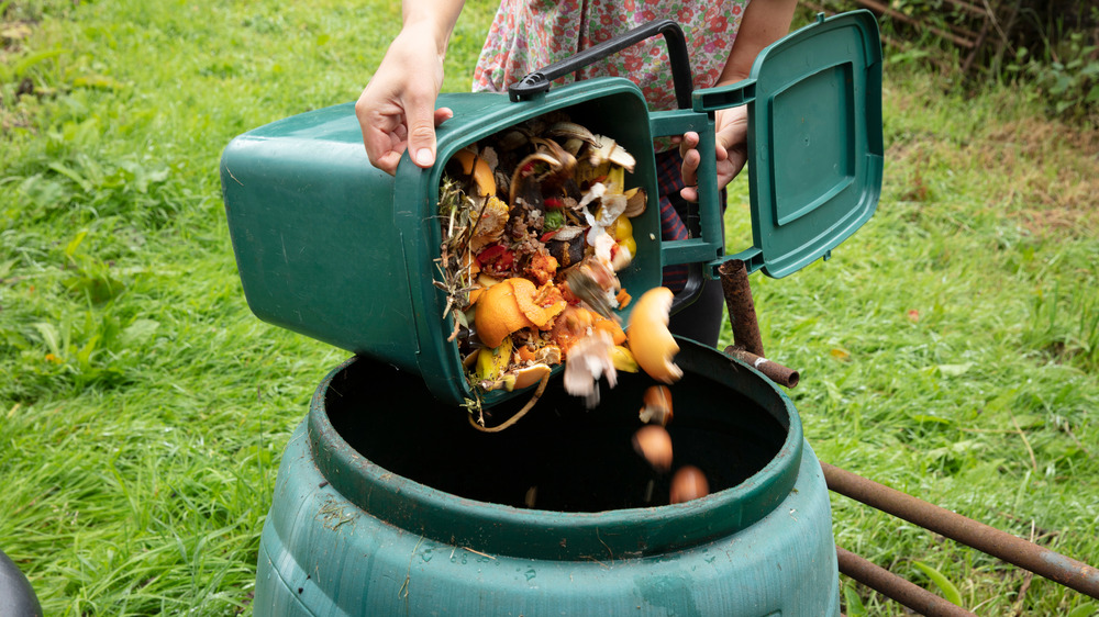 A woman emptying an indoor compost bin into a large bin outside