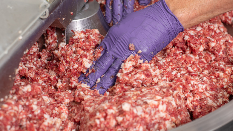 hands pushing ground pork in mixer