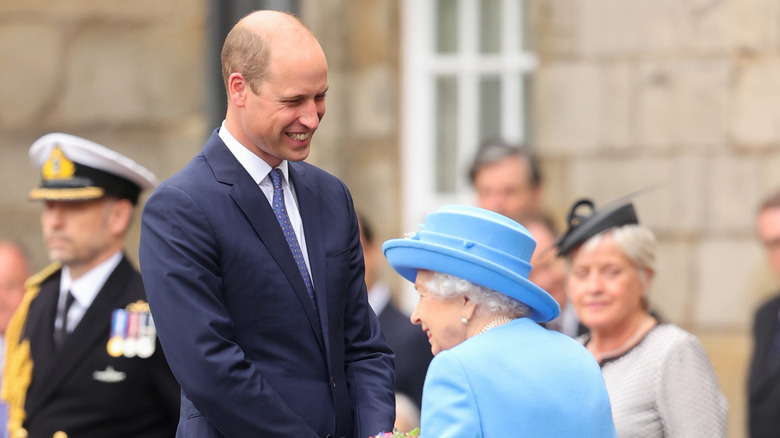 Prince William and the queen smiling and shaking hands