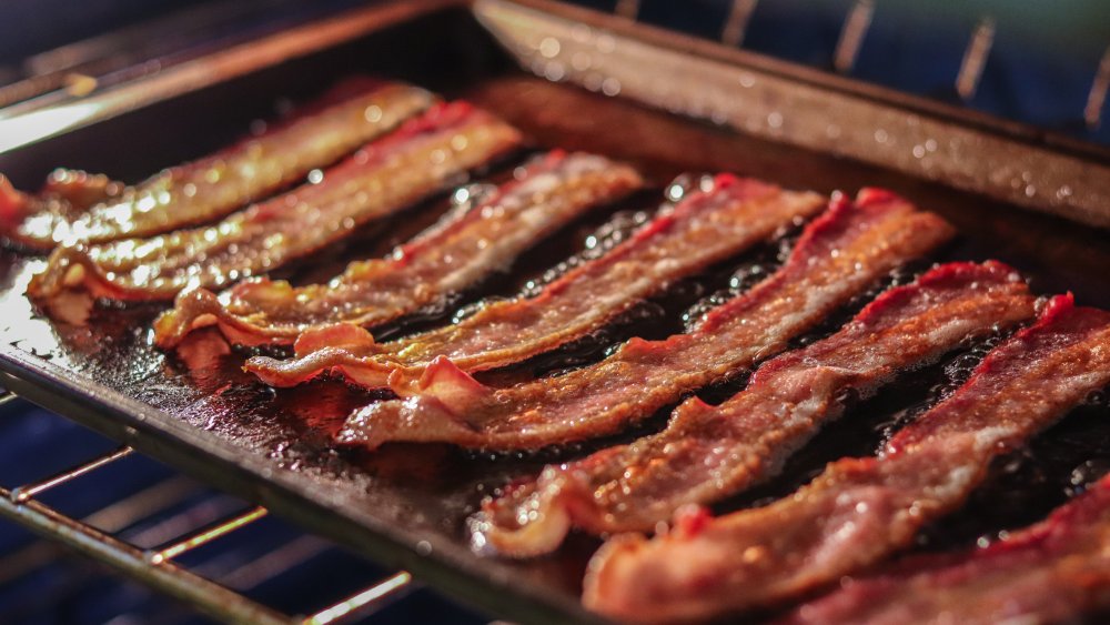 Bacon slices cooking on a cookie sheet, on an oven rack.