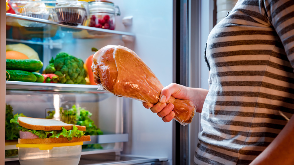 woman holding turkey leg in front of open refrigerator