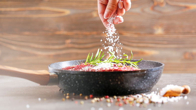 person salting a flank steak in a cast-iron pan